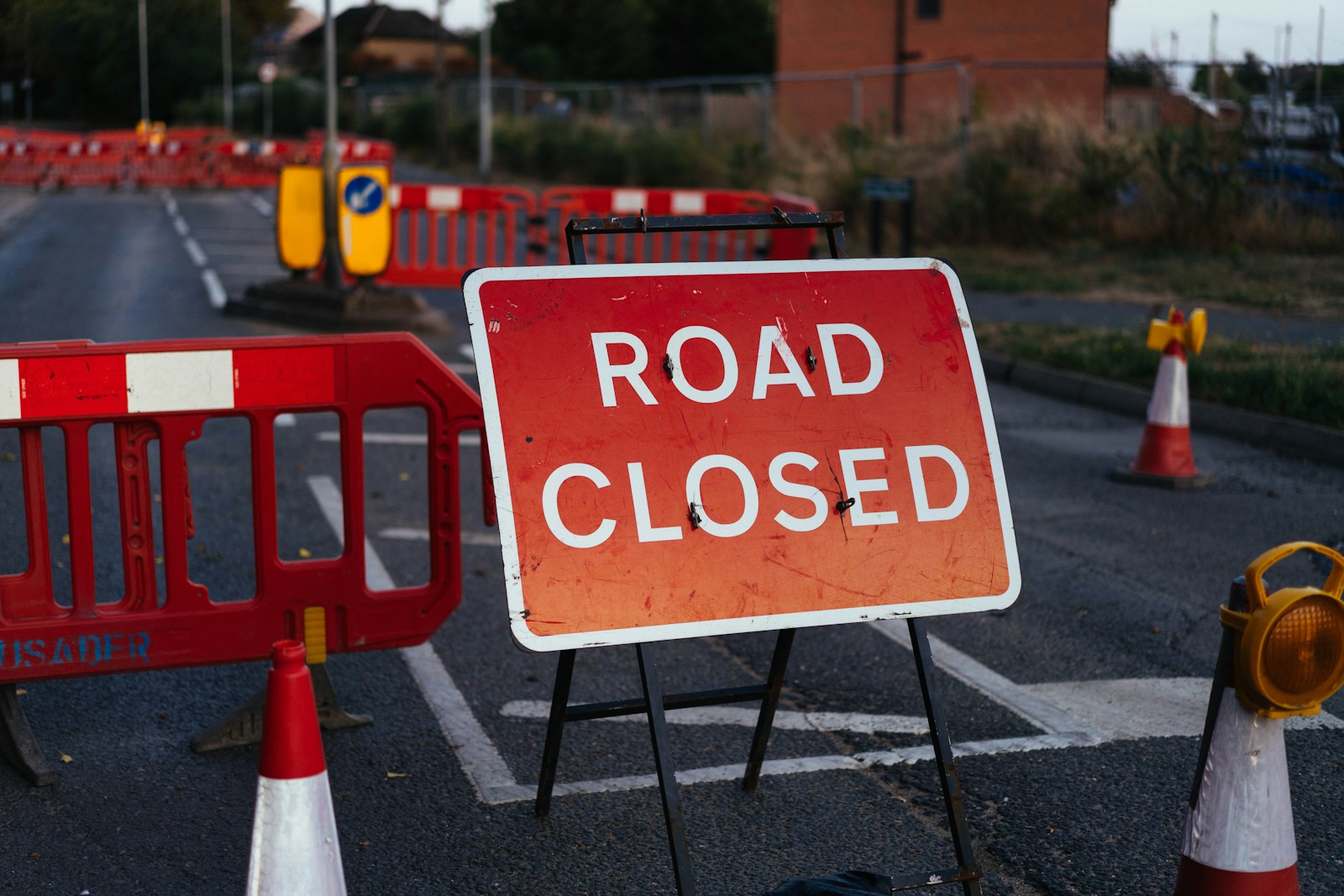A red road closed sign on a metal stand with orange barriers and traffic cones
